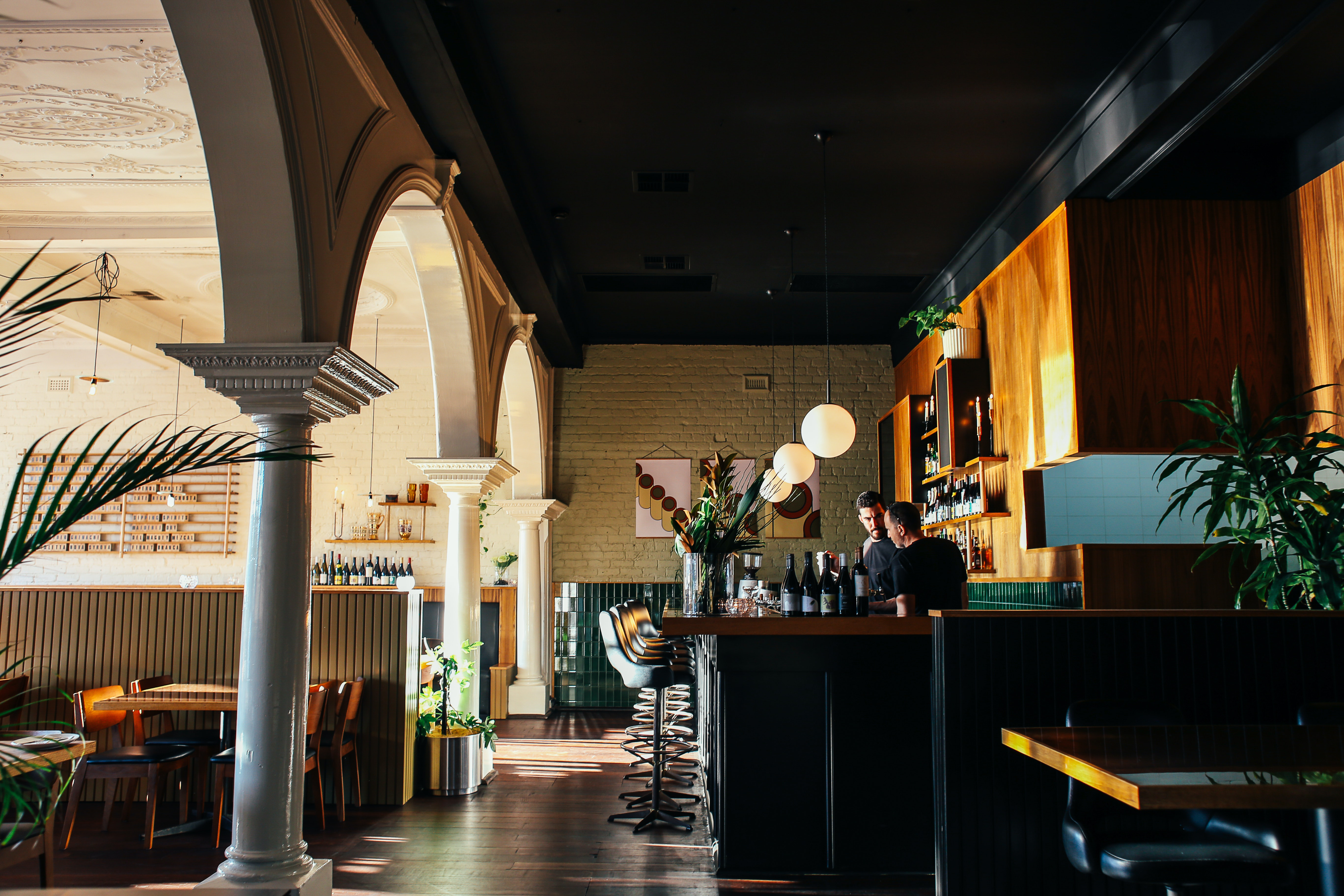 The inside of a bar, with arches to the left and a bar with bartenders to the right.