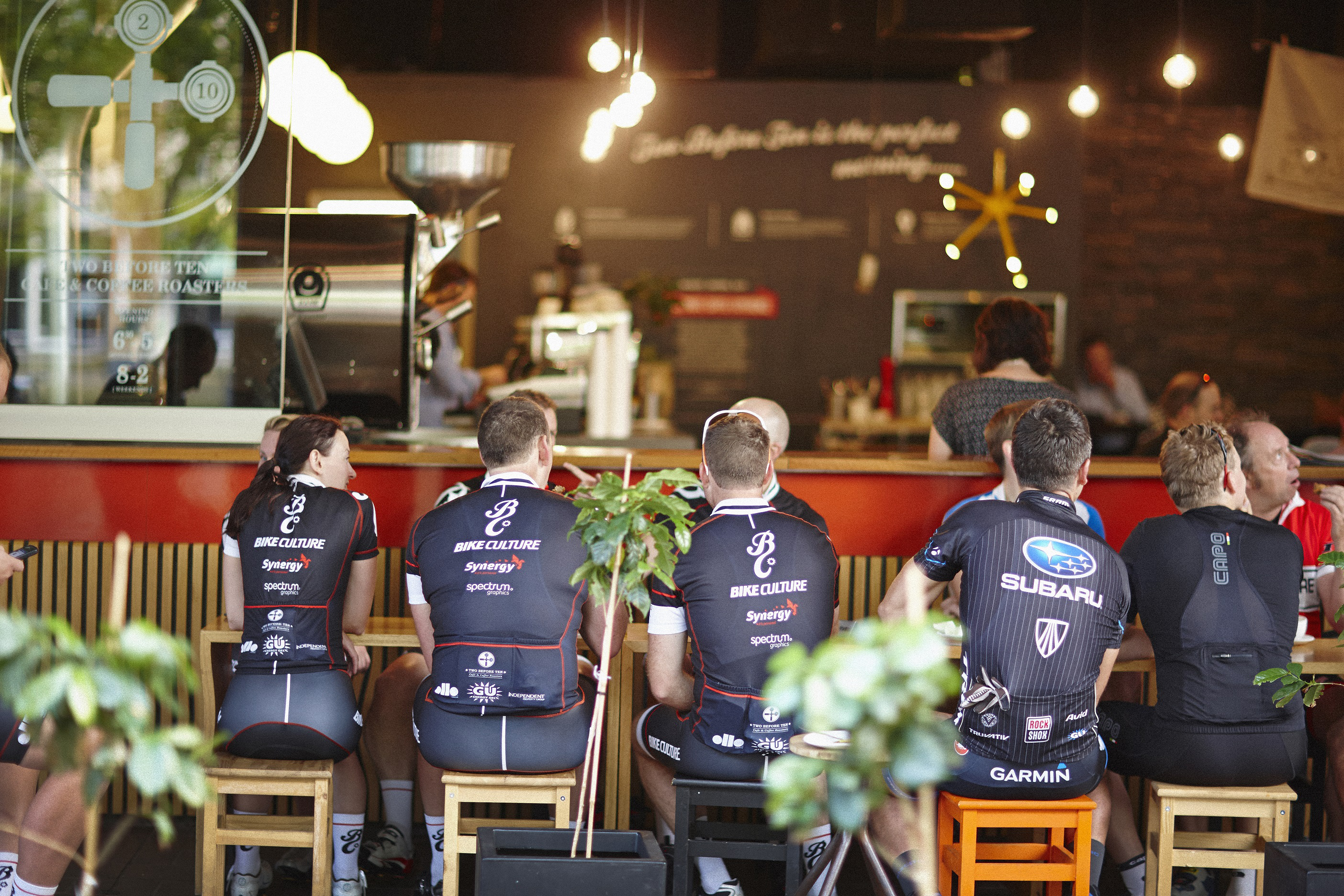 Cyclists in their spats sit around a table chatting and drinking coffee.