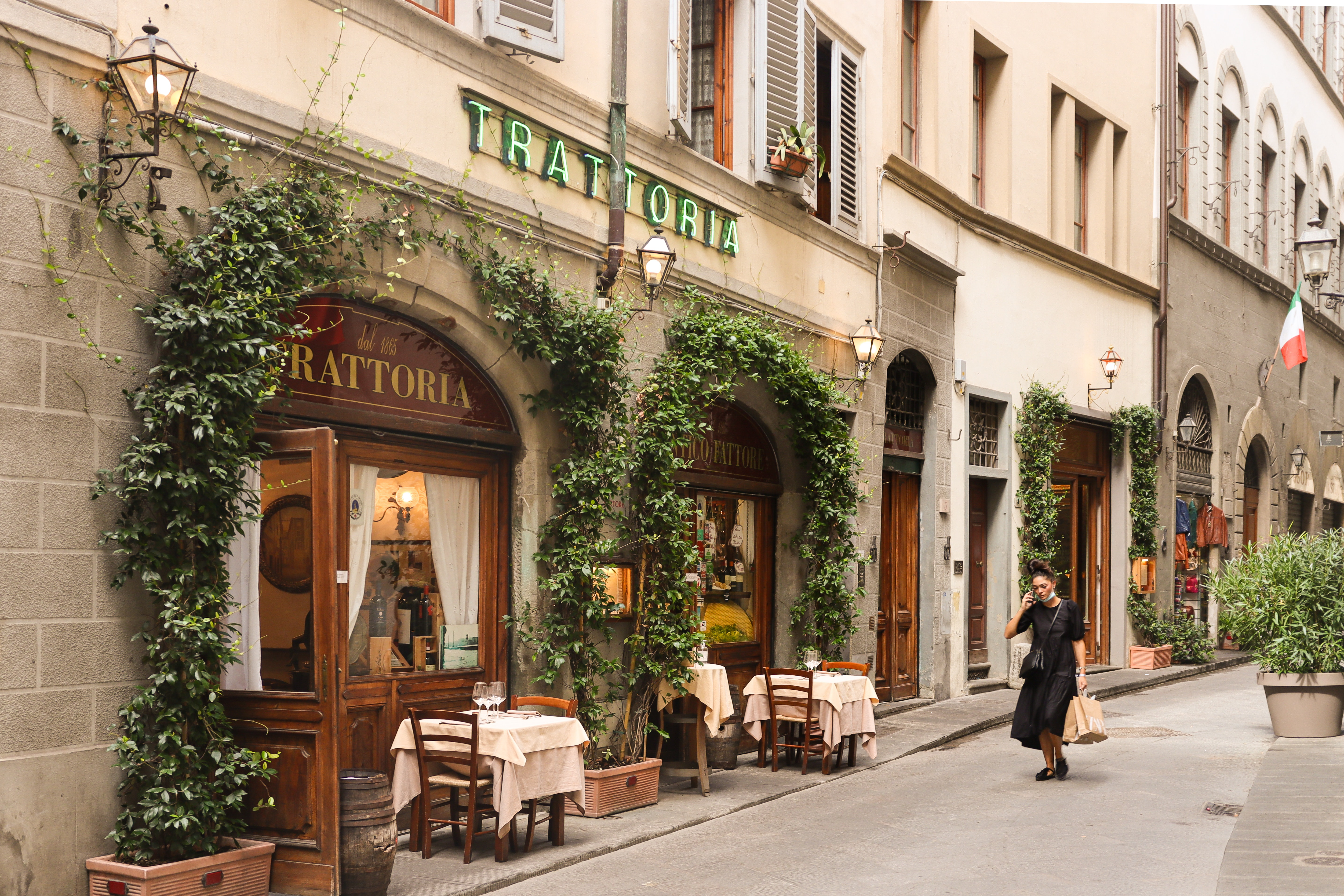 The outside of a trattoria covered in ivy on a cobblestone street.