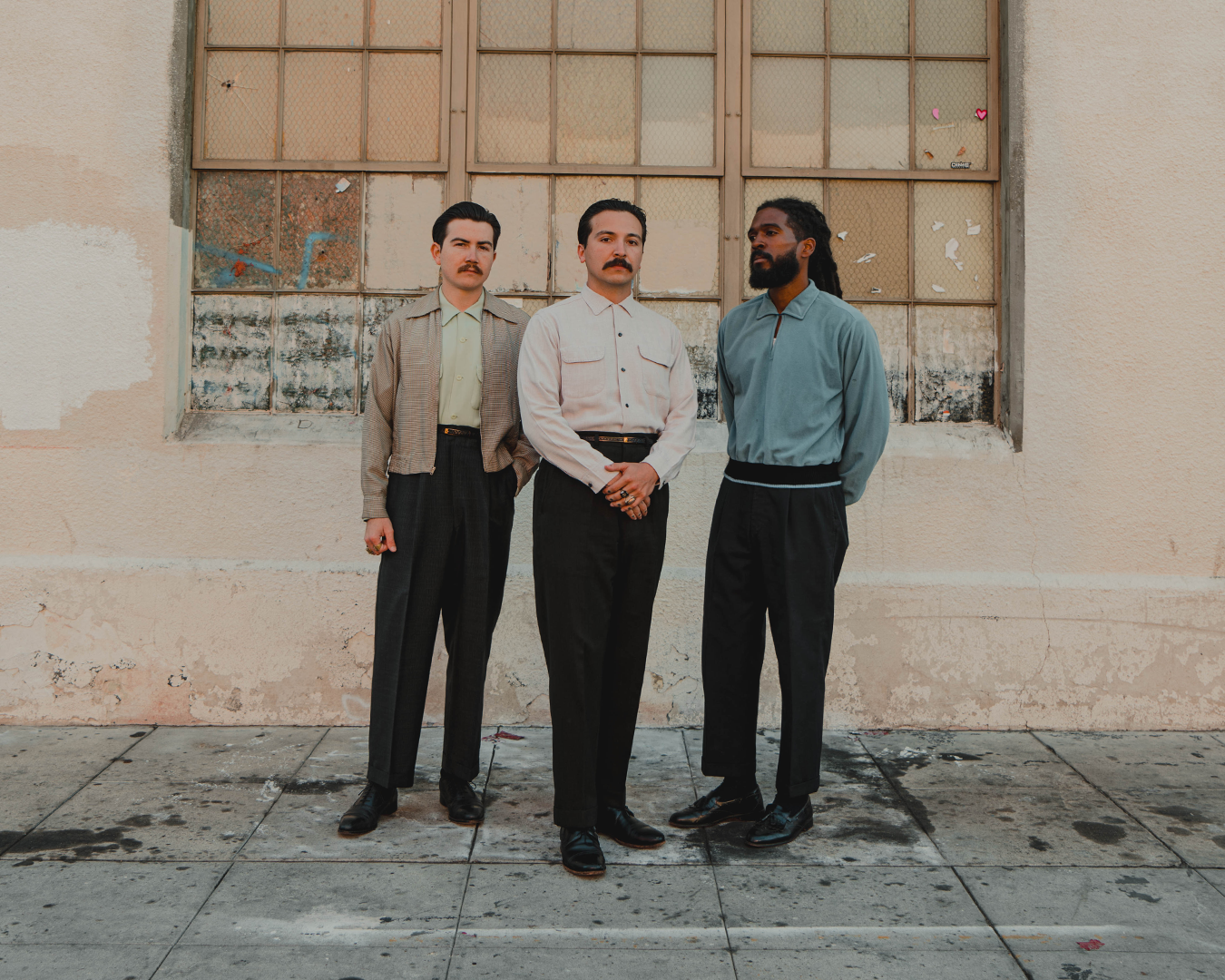 Thee Sacred Souls band members posing for a picture on a sidewalk in front of a tan building.