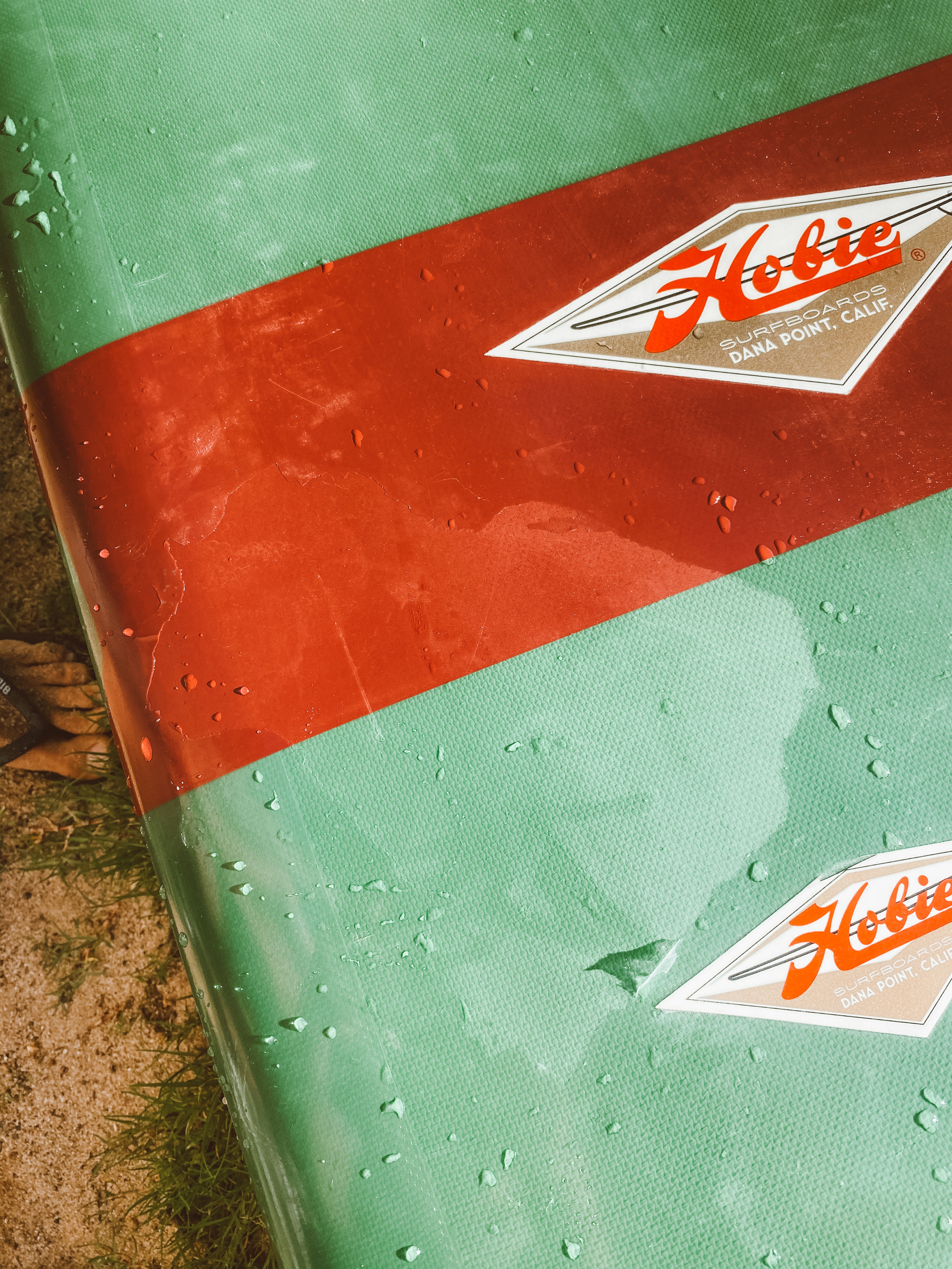 Surfboard close up with water droplets on its' shiny surface laying in the sand.