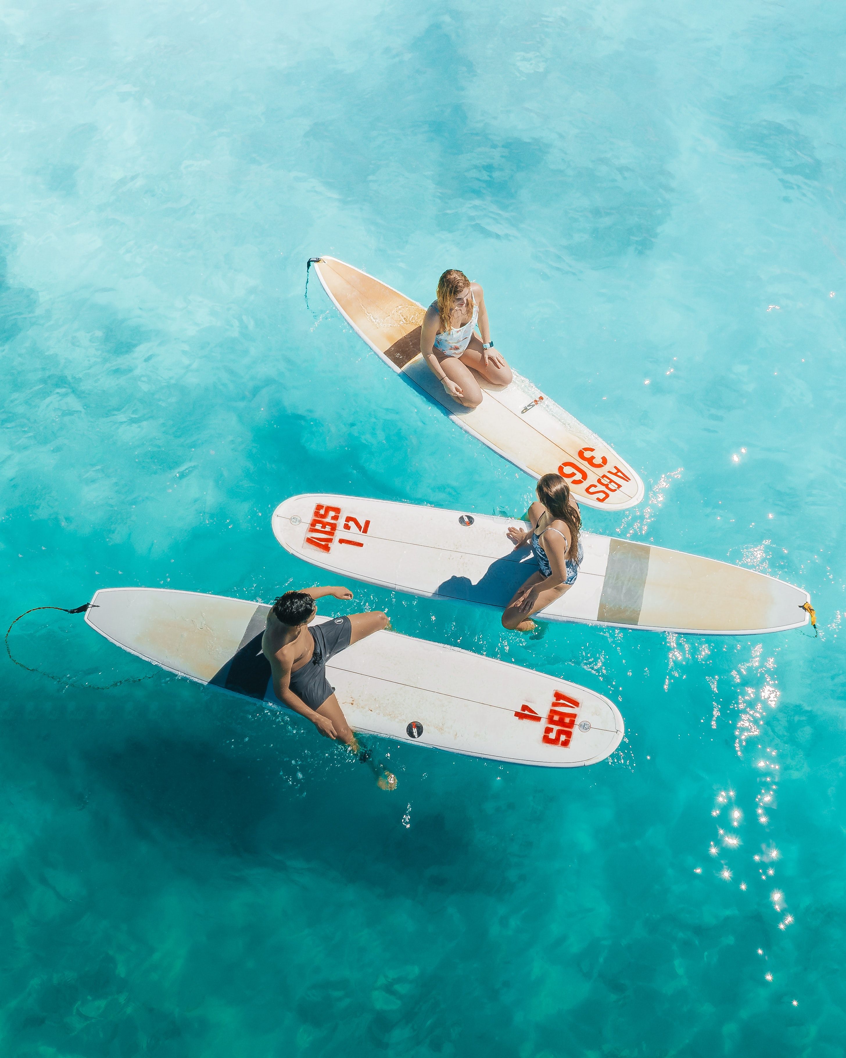 A birds eye view of 3 surfers in the water on their boards talking and looking towards the next wave.