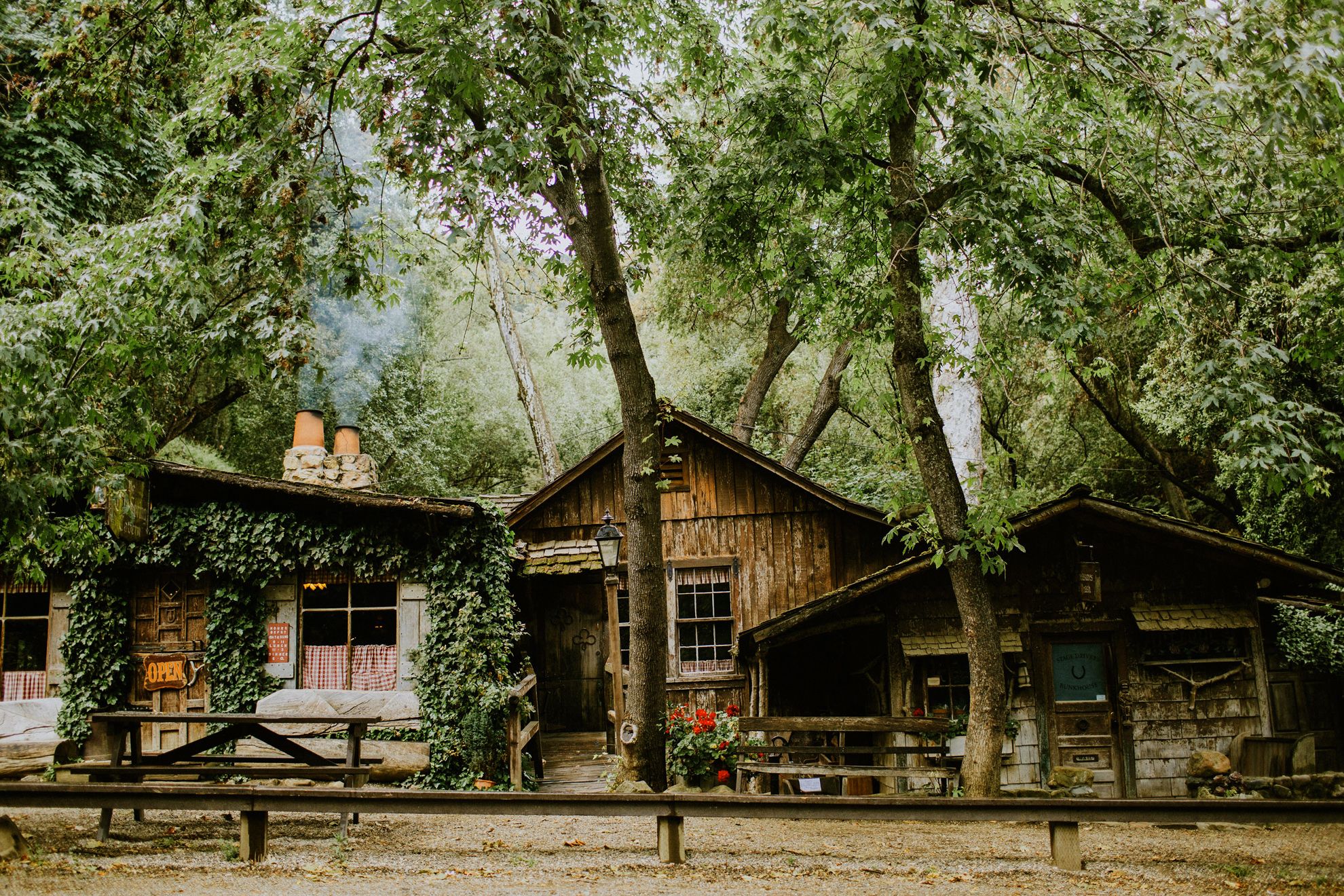 Front of Cold Springs Tavern, 3 wood cabin like buildings interspersed between trees.