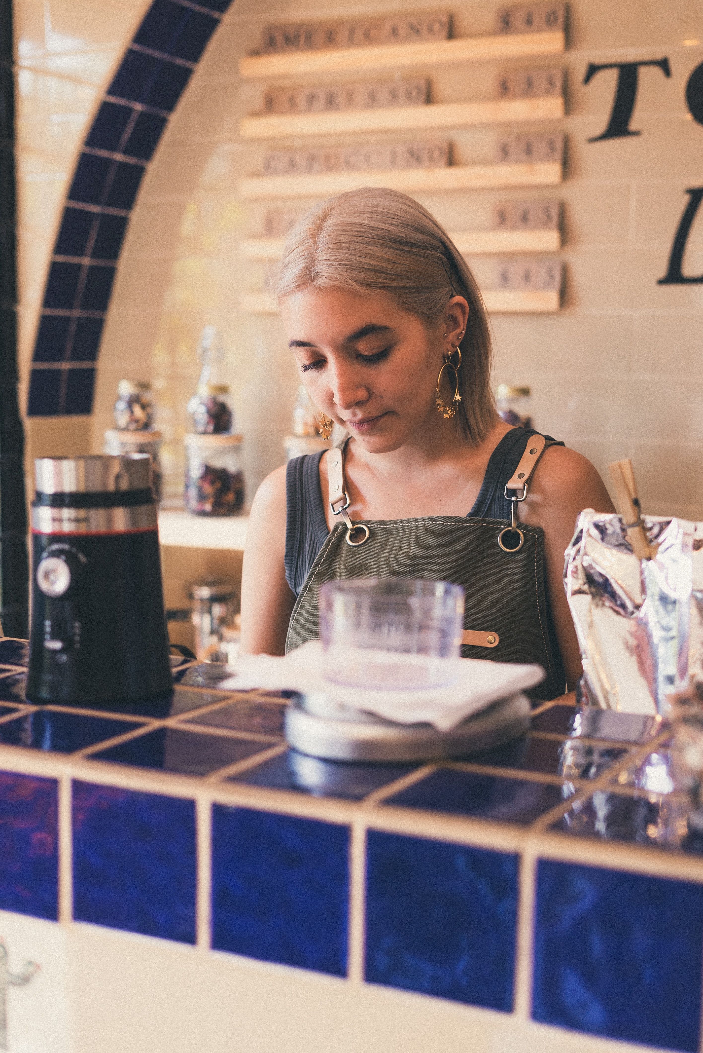 Female barista at tiled bar making coffee.