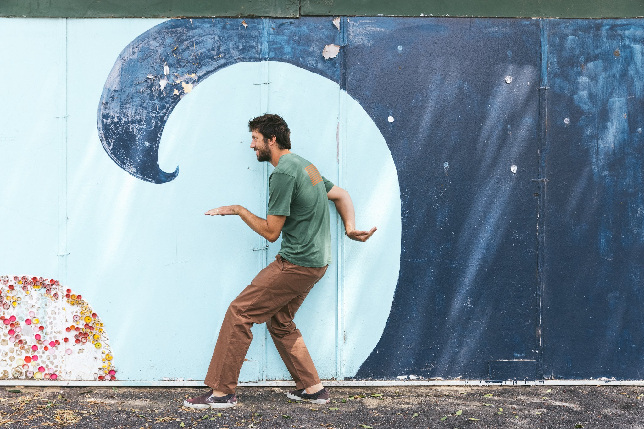 A man pretending to surf by posing next to a wave mural.